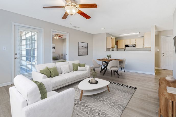 Light tan living room with wood-style flooring, a blue area rug, seating area, an open door to a bedroom at Cherry Grove Commons apartments in Sunset Beach, SC